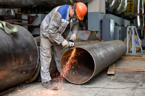 Fitter processes pipe edge with electric hand grinder Stock Photos