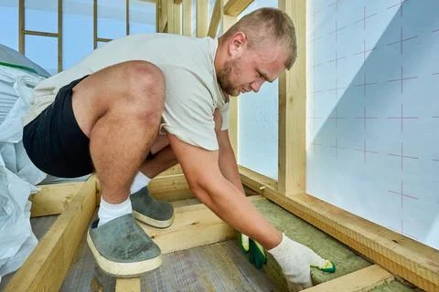 Fitting stone wool insulation between timber joists, male construction work.. Photos