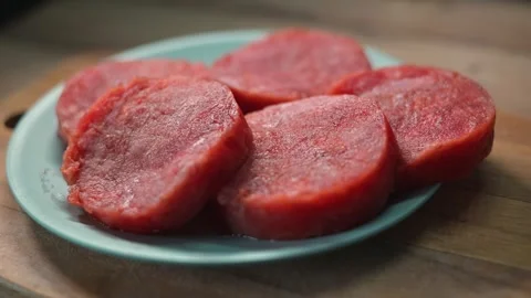 Five beef patties are neatly placed on a blue plate on a wooden countertop. Видео 338304054