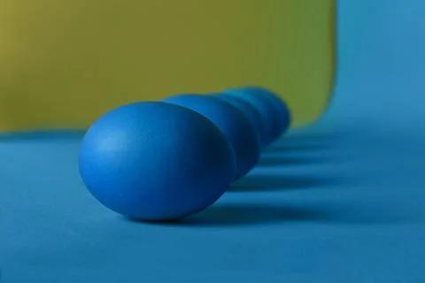 Five blue painted Easter eggs lie diagonally on a blue and yellow background Stock Photos