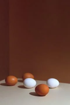 Five brown and white eggs with a hard shadow. They're in the corner of the bo Photos