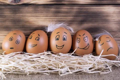 Five brown eggs with funny faces on a wooden background Stock-Fotos