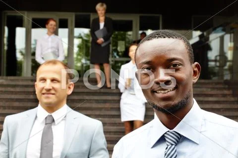 Five business people outdoors, the focus is on the smiling African American man Stock Photos