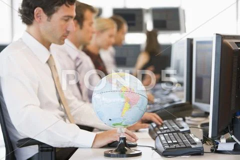 Five businesspeople in office space with a desk globe in foreground Stock Photos