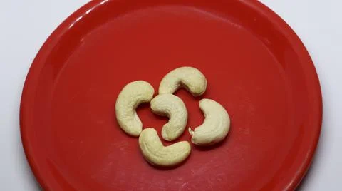 Five cashew nuts is on a white background on a red plate Stock Photos