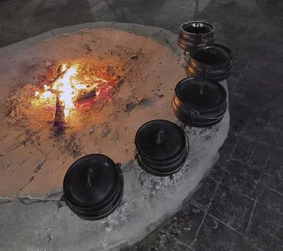 Five cast iron pots with lids sit over an open fire and coals. Foto stock