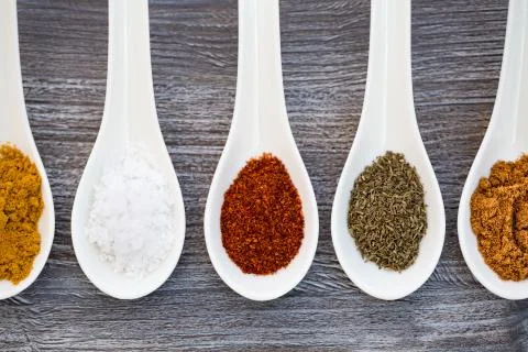 Five ceramic spoons lined up in a line filled with colorful spices on artific Stock Photos