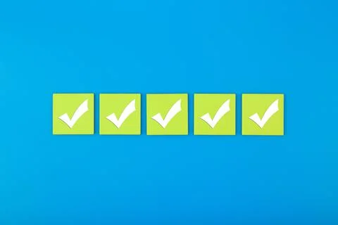 Five checkmarks on bright green tablets in the middle of blue background Stock Photos
