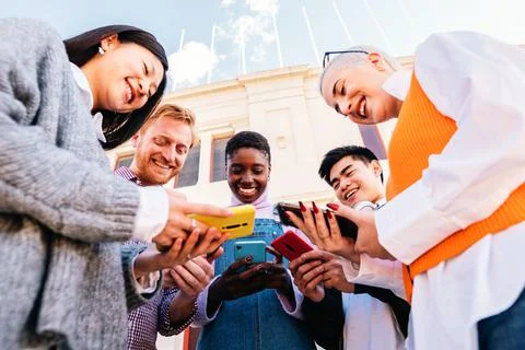 Five cherful friends using his cellphone and having fun together. Low angle of Stock Photos