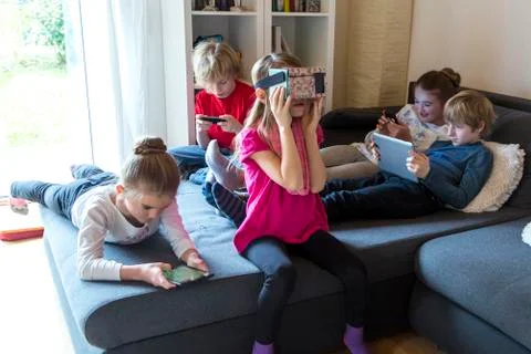 Five children on one couch using different digital devices Foto stock
