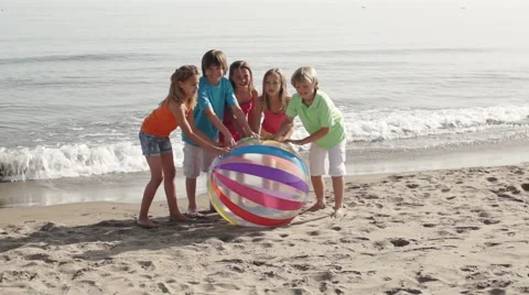 Five children running towards camera on beach pushing beach ball. Stock Footage 43672860