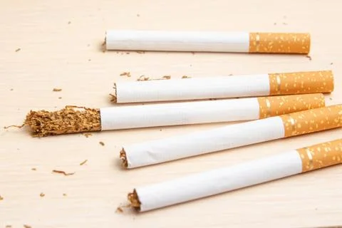 Five cigarettes and one got out on half tobacco on a light wooden Stock Photos