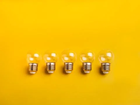 Five clear light bulbs lined up on yellow background. Concept of creative i.. Stock Photos