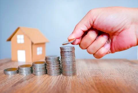 Five of coins stack with human hand on wooden table and house model Stock Photos