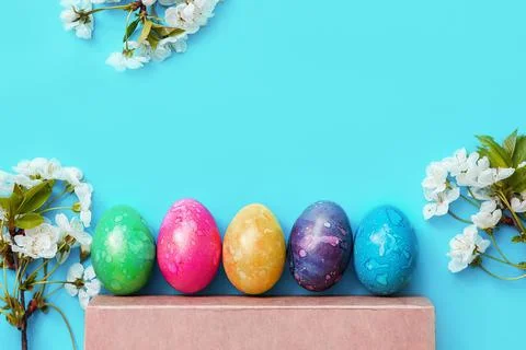 Five colorful easter eggs and flowers on blue background. Stock Photos