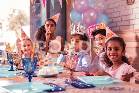 Five cute children sitting at the table and blowing party horns Stock Photos