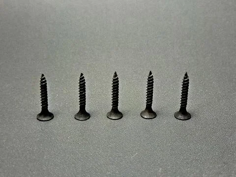 Five dark screws stand aligned on a gray textured surface in a still life a.. Stock Photos