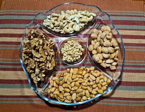 Five different types of nuts on a special glass plate are served for dessert Stock Photos