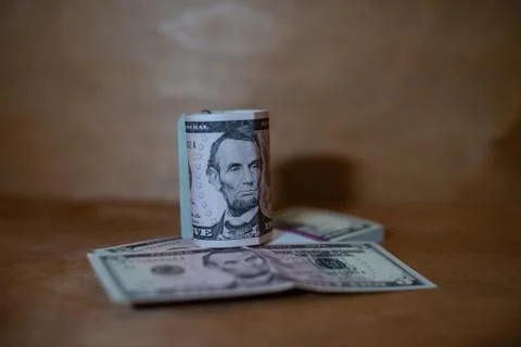 Five dollar bills in a roll lying on a bundle of banknotes. Stock Photos