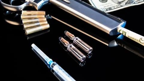 Five dollars in a pistol on a black table with a syringe and cartridges.Sale, Foto stock