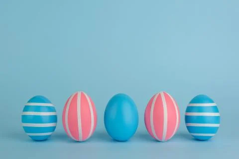 Five Easter blue and pink eggs with white stripes on blue background. Stock Photos