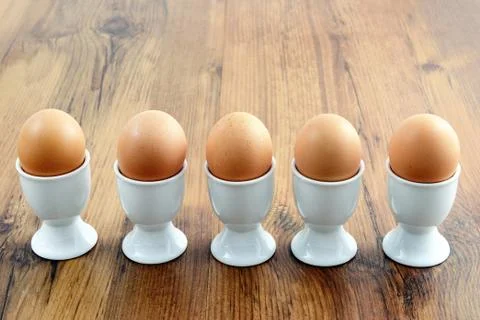 Five egg cups with natural brown eggs in a row on table Foto stock