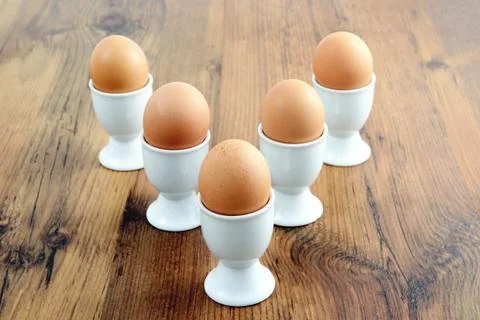 Five egg cups with natural brown eggs in arrow shape on table Stock Photos
