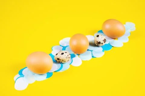 Five eggs on white and blue confetti and yellow background. Stock Photos