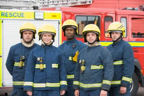 Five firefighters standing by fire engine wearing helmets Stock Photos