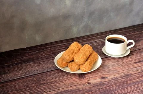 Five fresh eclairs with sprinkles and a cup of black coffee on a wooden table Stock Photos