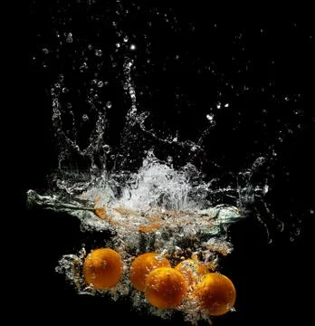 Five fresh oranges falling in water on a dark background Stock Photos