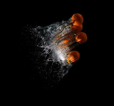 Five fresh oranges falling in water on a dark background Stock Photos