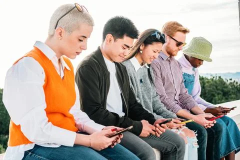 Five friends browsing in internet with their smartphones sitting together Stock Photos