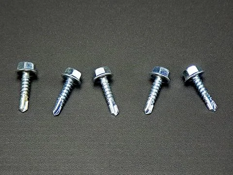 Five galvanized hex head self-drilling screws arranged evenly on dark textu.. Stock Photos