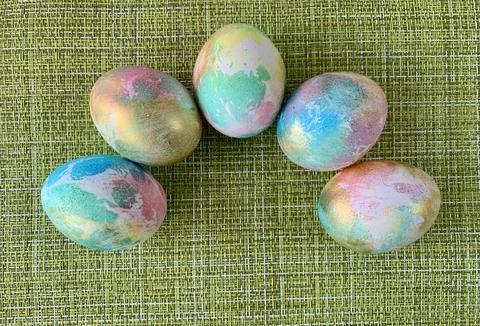 Five hand-dyed easter eggs with vibrant pastel colors sit neatly on a textured Stock-Fotos