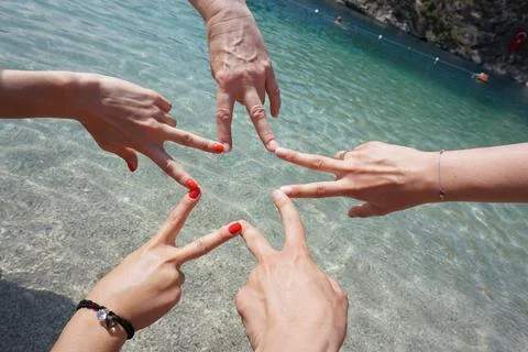 Five hands building a star shape by finger connection in front of sea. Happy Stock Photos