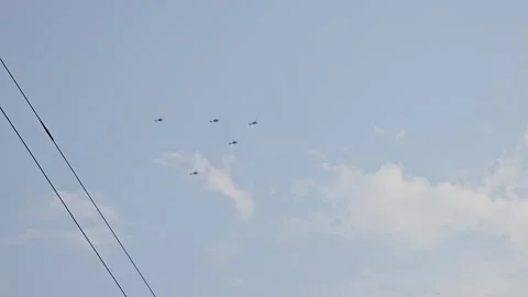 Five helicopters fly in formation above dark power lines, crossing into the open 库存影片 336440827