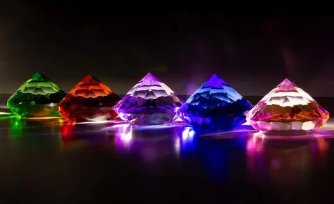Five illuminated diamond-shaped crystals, each with a distinct color Foto stock