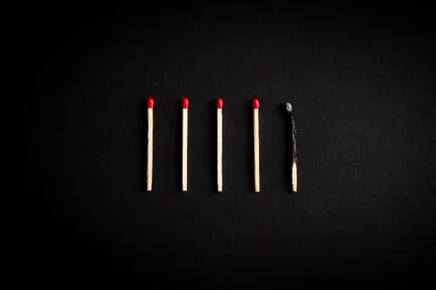 Five matches on a black background. One burned. Stock Photos