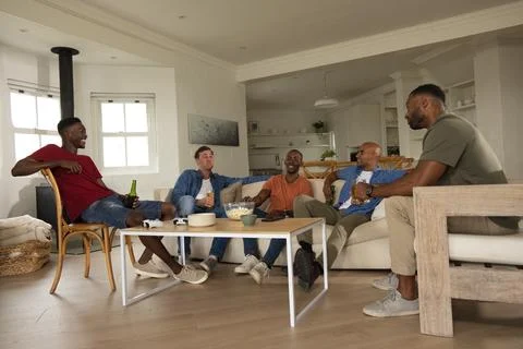 Five men laughing, holding drinks and chatting on sofa at home with snacks, Stock Photos