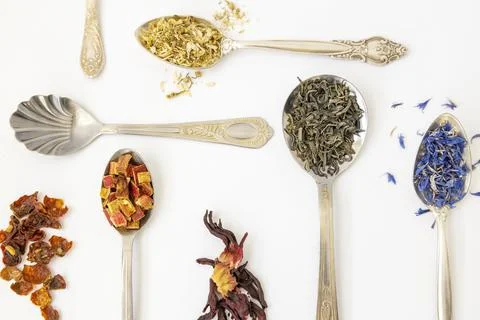 Five metal spoons with different types of tea, close up, on a white background. Stock Photos