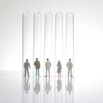 Five miniature figurines stand inside tall, empty test tubes on a reflectiv.. Stock Photos