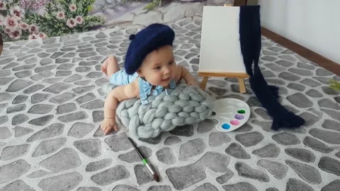 A five-month-old artist boy  lying on a pavement with a palette and easel Stock Footage 157126360