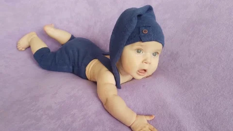A five-month-old boy in a blue gnome costume lies on a purple bedspread Stock Footage 157207494