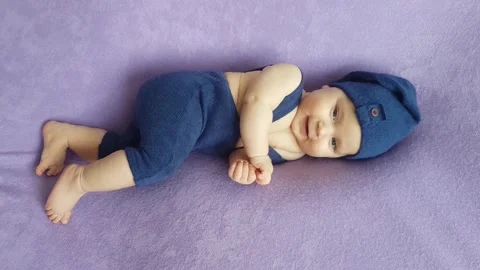 A five-month-old boy in a blue gnome costume lies on a purple bedspread Stock Footage 157207497