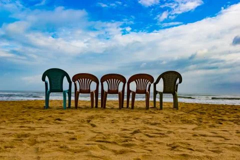 Five multi cloured chair on a sandy beach with blue sky in a sunny day perfec Stock Photos