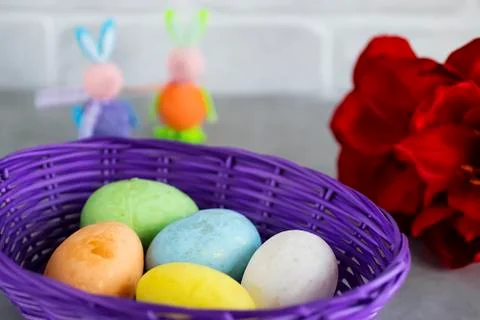 Five multicolored decorative eggs in  purple basket, two decorative rabbits a Stock Photos