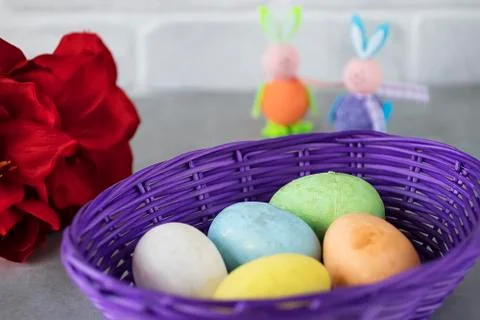 Five multicolored decorative eggs in  purple basket, two decorative rabbits a Stock Photos