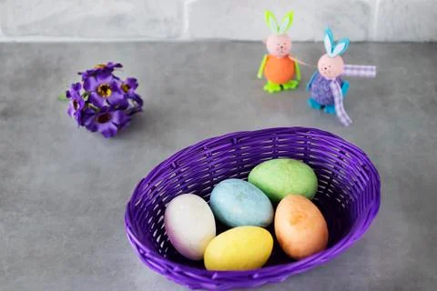 Five multicolored decorative eggs in  purple basket, two decorative rabbits a Stock Photos