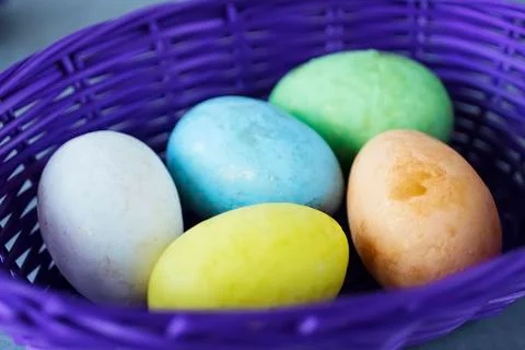 Five multicolored decorative eggs in a purple basket on a gray background. Ea Stock Photos